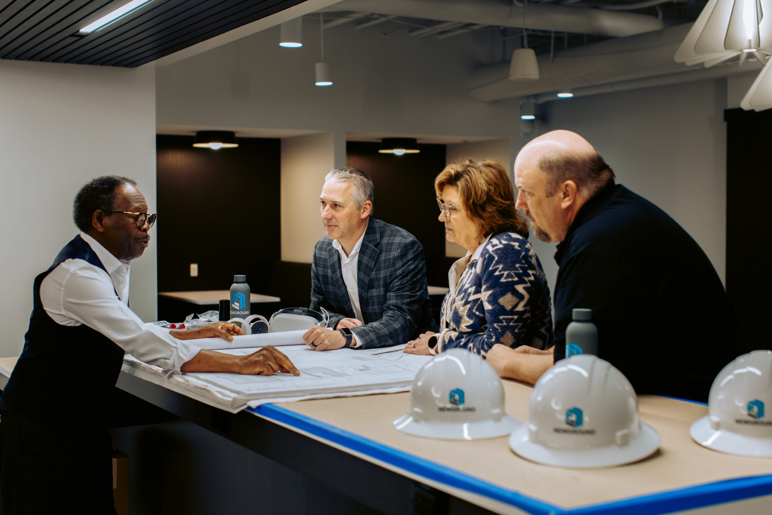 NewGround team meeting around a table with construction plans and hard hats on the table