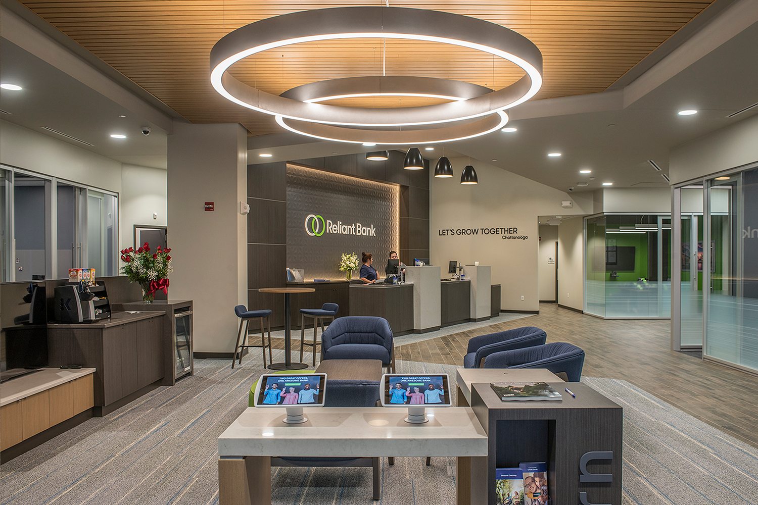 Reliant Bank lobby with a table with two technology tablet stations, sitting areas, a counter and two employees in the background