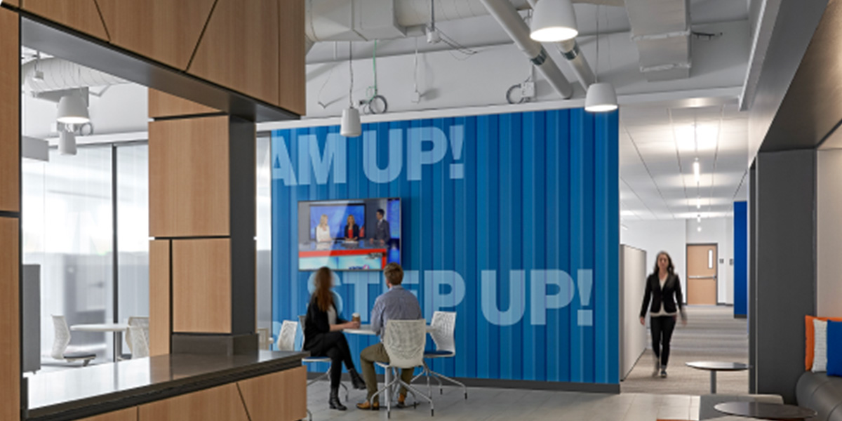 branded wall with large screen hanging on it and a table and chairs in front of it